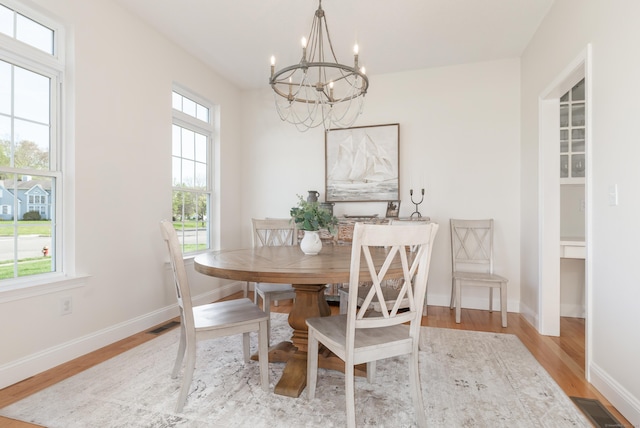 dining space with an inviting chandelier, baseboards, wood finished floors, and visible vents