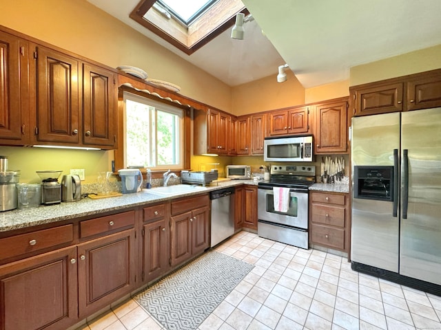 kitchen featuring a sink, brown cabinetry, stainless steel appliances, light tile patterned floors, and a skylight