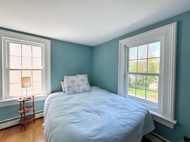 bedroom with a baseboard radiator, multiple windows, a baseboard heating unit, and wood finished floors
