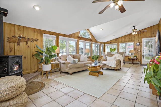 living room featuring wooden walls, a ceiling fan, light tile patterned floors, and a wood stove
