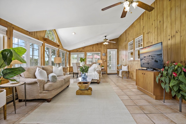 living area featuring a ceiling fan, light tile patterned floors, lofted ceiling, and wooden walls