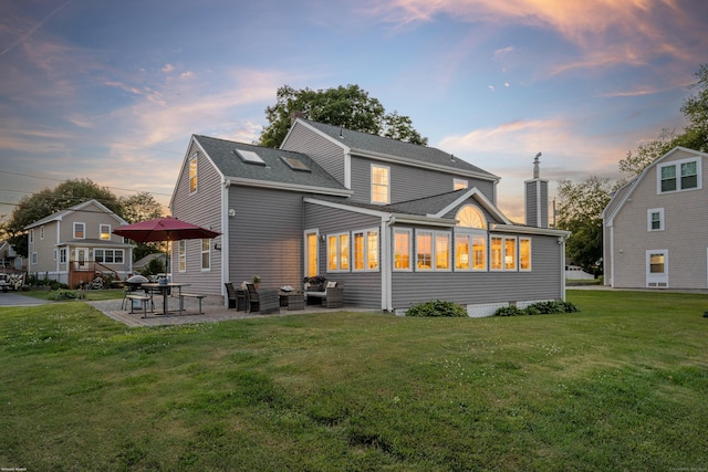 back of house at dusk with a lawn, a patio, and a chimney