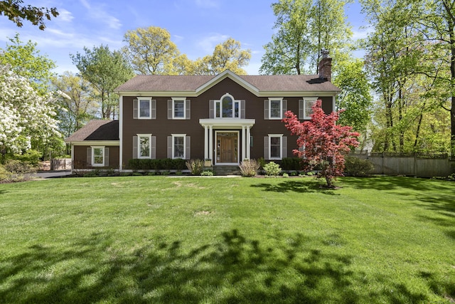 colonial inspired home with fence, a chimney, and a front lawn