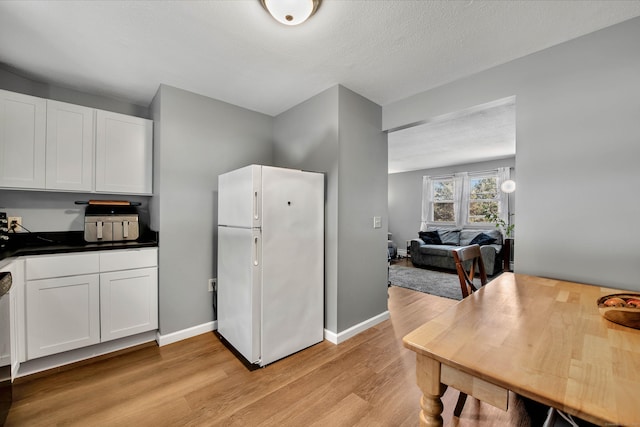 kitchen featuring freestanding refrigerator, dark countertops, light wood-style floors, baseboards, and white cabinetry