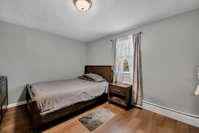 bedroom featuring a textured ceiling, baseboards, a baseboard heating unit, and wood finished floors