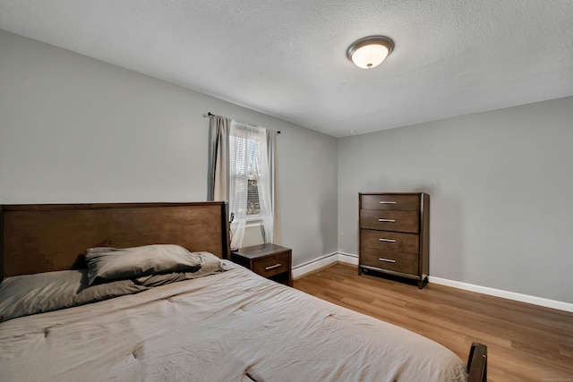 bedroom featuring baseboards, a textured ceiling, a baseboard heating unit, and wood finished floors
