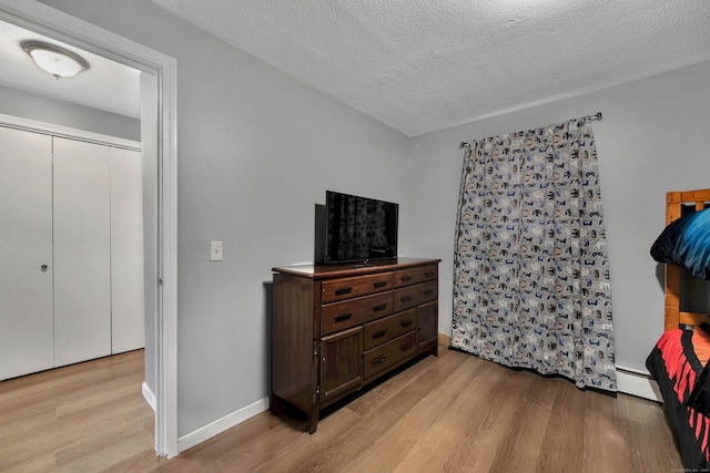 bedroom with baseboards, a baseboard radiator, light wood-style flooring, and a textured ceiling