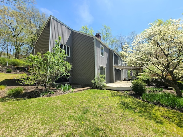 back of house featuring a wooden deck, a chimney, and a lawn