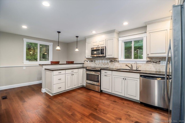 kitchen with dark countertops, stainless steel appliances, a peninsula, and a sink