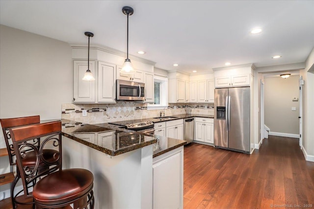 kitchen featuring decorative light fixtures, a peninsula, backsplash, white cabinets, and appliances with stainless steel finishes