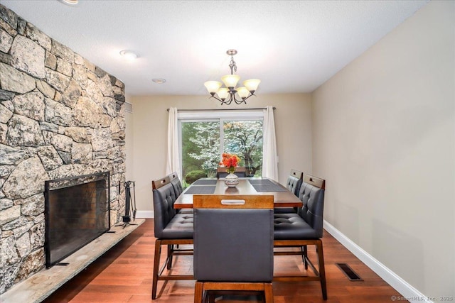 dining area with a stone fireplace, a notable chandelier, visible vents, and wood finished floors