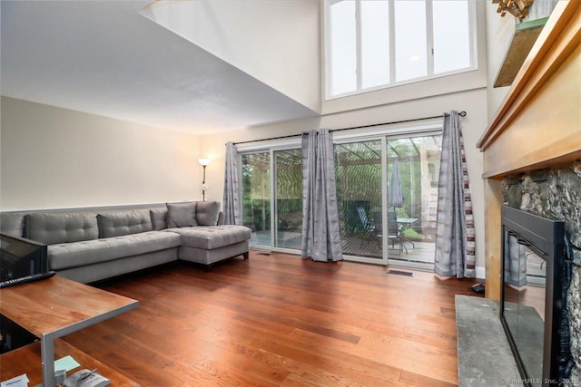 living room featuring a glass covered fireplace, visible vents, a towering ceiling, and wood finished floors