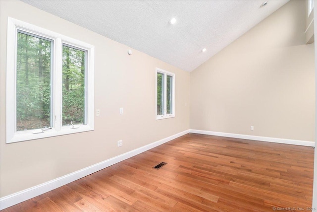 spare room with vaulted ceiling, visible vents, light wood finished floors, and baseboards
