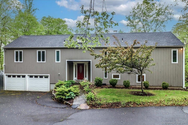 bi-level home featuring roof with shingles, a garage, a front lawn, and driveway