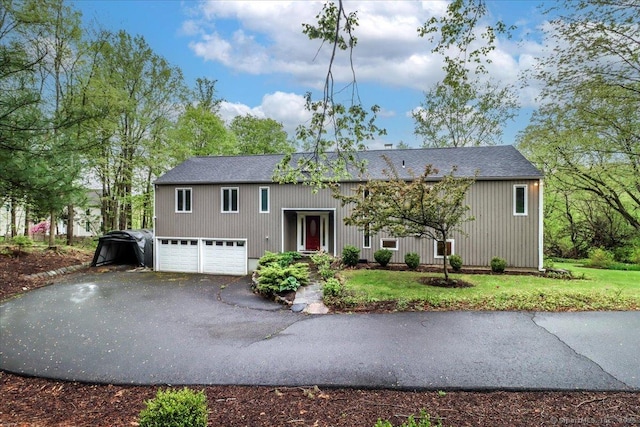 bi-level home with driveway, a shingled roof, an attached garage, and a front yard