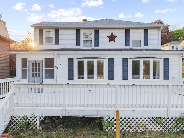 view of front of house with a wooden deck, roof with shingles, and a chimney