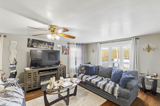 living area featuring a glass covered fireplace, a ceiling fan, and wood finished floors