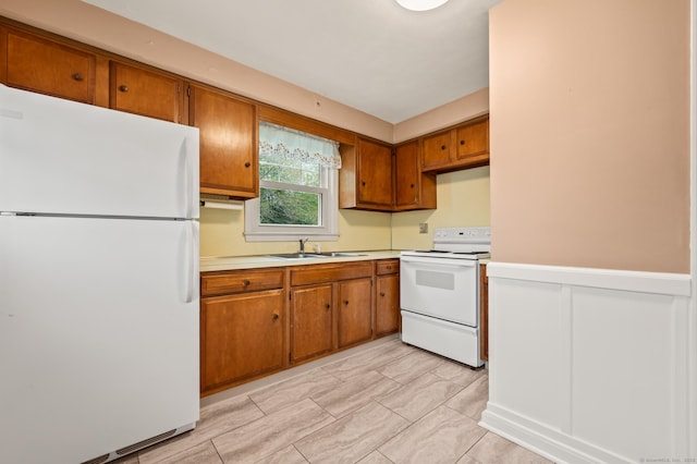 kitchen featuring brown cabinetry, a sink, and white appliances