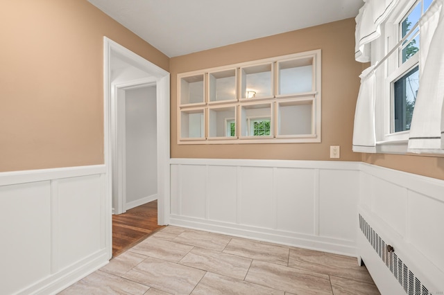 spare room with wainscoting, radiator, light wood-style floors, and a decorative wall