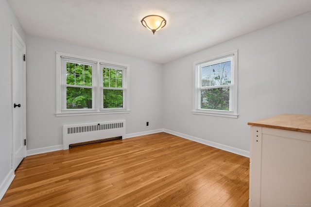 spare room with baseboards, a healthy amount of sunlight, radiator heating unit, and light wood-type flooring