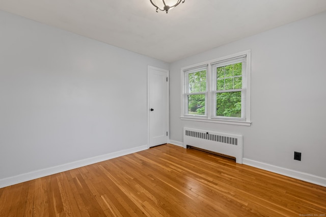 spare room with baseboards, light wood-style floors, and radiator heating unit