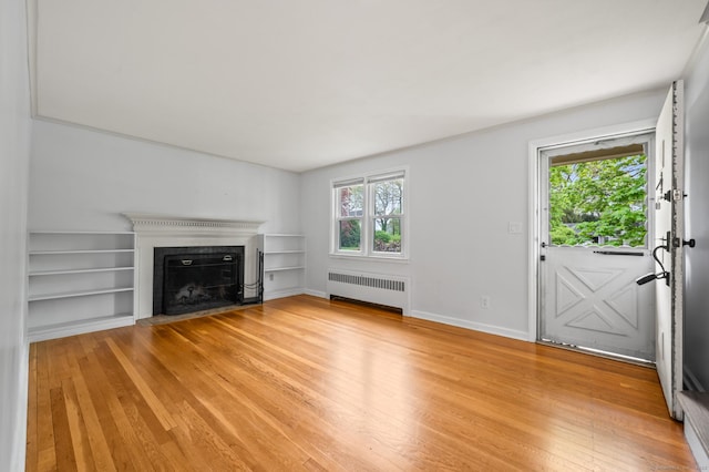 unfurnished living room featuring radiator heating unit, built in shelves, light wood-style floors, and a fireplace with flush hearth