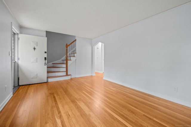 unfurnished living room with stairway, baseboards, and light wood finished floors