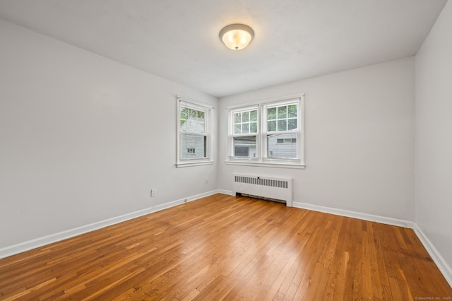empty room with baseboards, radiator heating unit, and hardwood / wood-style flooring