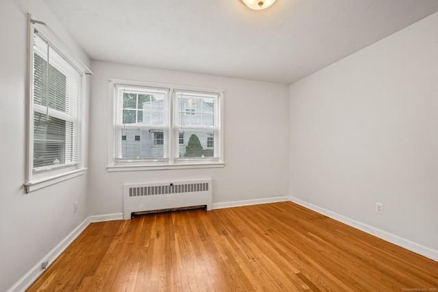 unfurnished room with radiator, baseboards, and light wood-style flooring