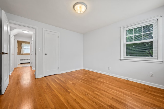 spare room with baseboards, radiator heating unit, and light wood-type flooring
