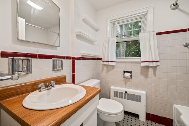bathroom featuring vanity, toilet, radiator heating unit, a wainscoted wall, and tile walls