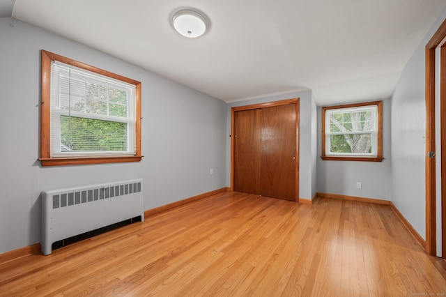 unfurnished bedroom with a closet, light wood finished floors, radiator heating unit, and multiple windows