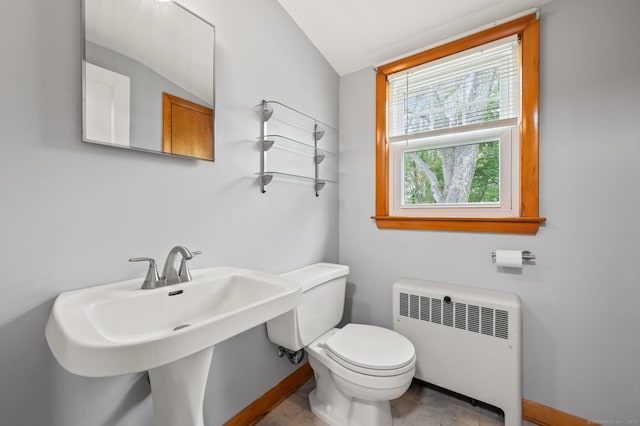 bathroom featuring lofted ceiling, toilet, baseboards, radiator heating unit, and a sink