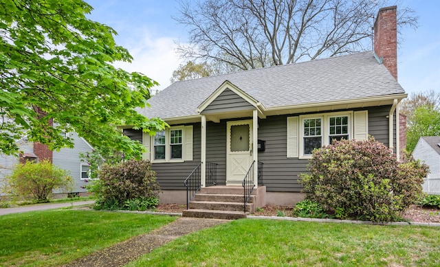 view of front of house with entry steps, a chimney, a shingled roof, and a front yard