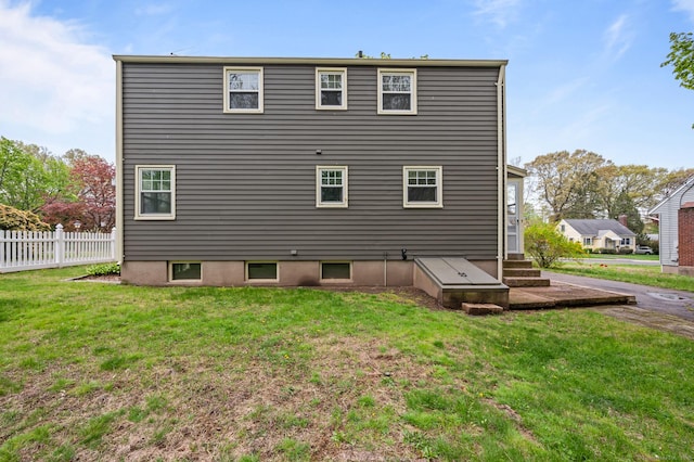 rear view of property featuring fence, entry steps, and a lawn