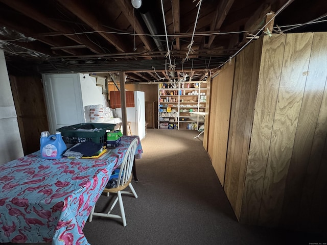 unfinished basement featuring wood walls, carpet, and freestanding refrigerator