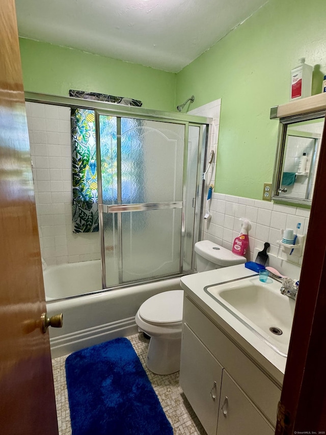 bathroom featuring tile walls, wainscoting, vanity, toilet, and shower / bath combination with glass door