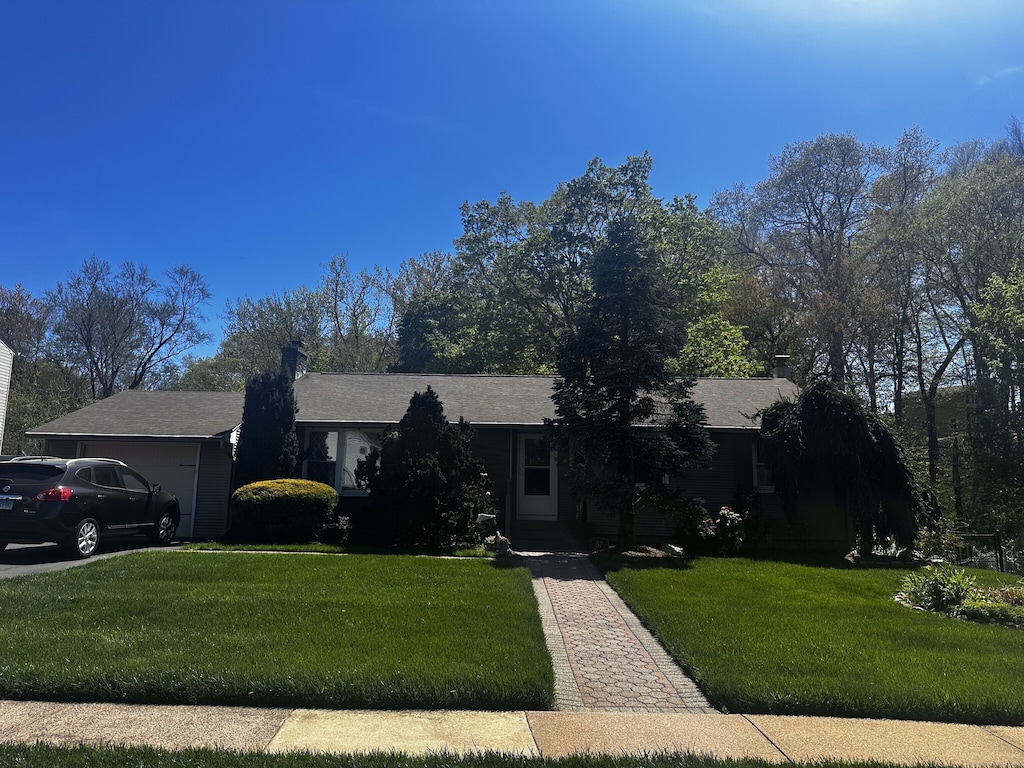 ranch-style home with a garage, a chimney, and a front yard