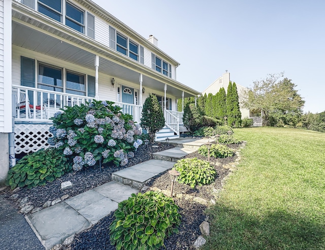 view of front of house with covered porch, a chimney, and a front lawn