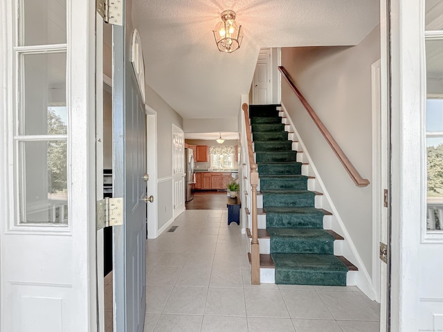 stairway with a textured ceiling, tile patterned floors, an inviting chandelier, and a wainscoted wall