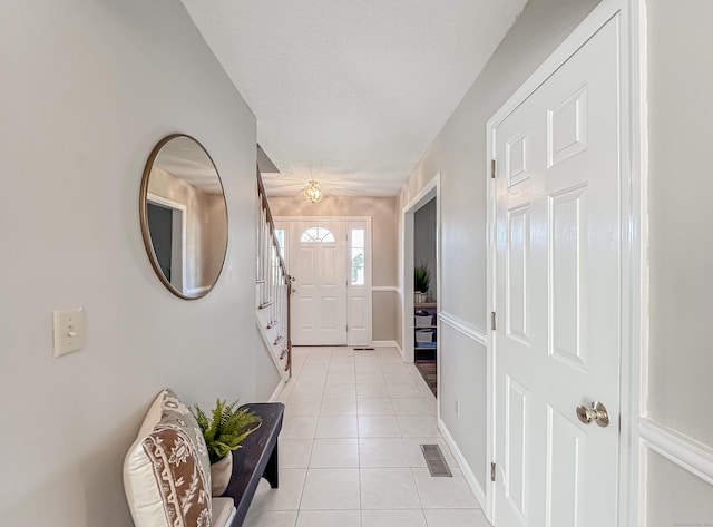 foyer entrance featuring visible vents, baseboards, light tile patterned floors, and stairway