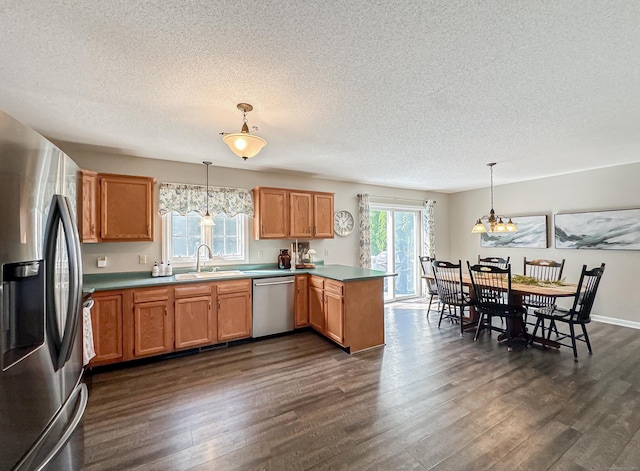kitchen with a textured ceiling, appliances with stainless steel finishes, dark wood finished floors, a sink, and a peninsula