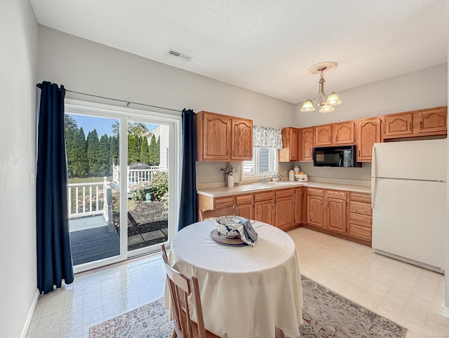 kitchen featuring visible vents, black microwave, light countertops, freestanding refrigerator, and an inviting chandelier