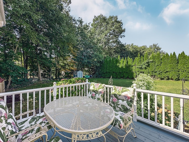 wooden deck featuring a storage shed, a yard, outdoor dining space, and an outbuilding