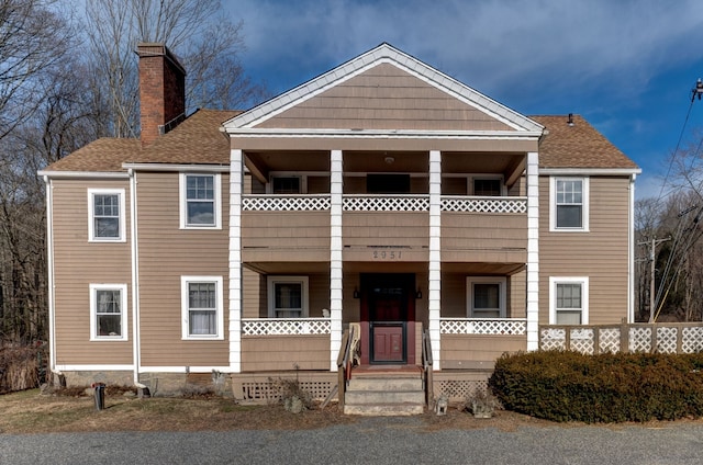 greek revival inspired property featuring a porch, a chimney, a balcony, and roof with shingles