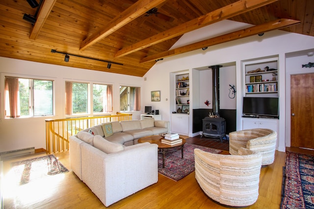 living room featuring lofted ceiling with beams, a baseboard heating unit, built in features, wood ceiling, and a wood stove