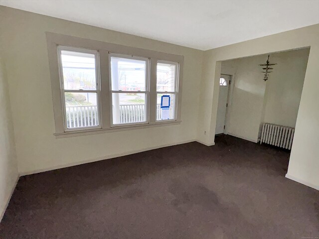 spare room with radiator heating unit and dark carpet