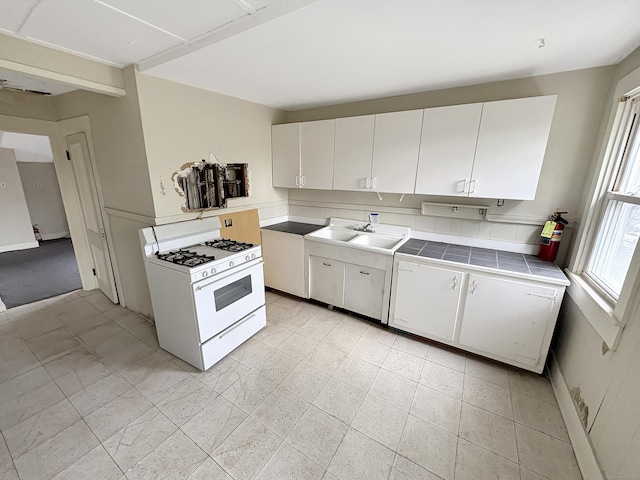 kitchen with white gas range, tile counters, a sink, and white cabinets