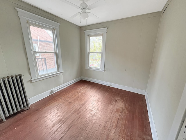 empty room with wood-type flooring, a ceiling fan, radiator, and baseboards
