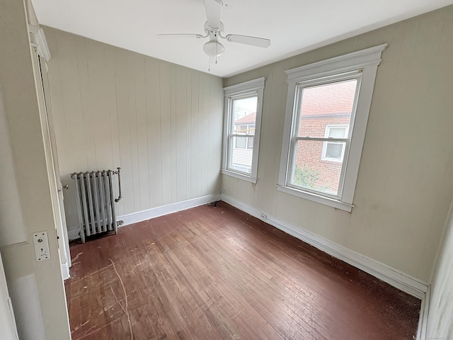 unfurnished room with a ceiling fan, baseboards, radiator, and dark wood-type flooring